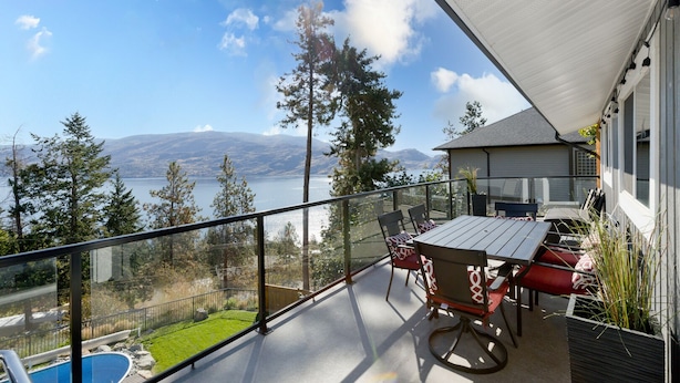 A balcony with a table and chairs, overlooking a lake and mountains. - Vacation for Families with Stunning View & Pool (Peachland)