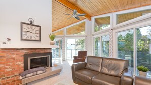 A spacious living room with a fireplace, leather sofa, and large windows offering a view of the outdoors. - Vacation for Families with Stunning View & Pool (Peachland)