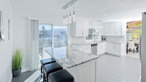A modern kitchen with a large island, white cabinetry, and a view of the outdoors. - Vacation for Families with Stunning View & Pool (Peachland)