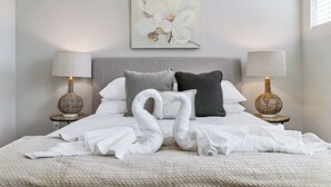 A neatly made bed with two white towels arranged in a swan shape, a grey and black pillow, and a white floral painting above the bed.