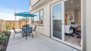A patio with a table and chairs, a blue umbrella, and a sliding glass door leading to an interior dining area.