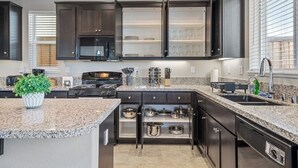 A modern kitchen with dark cabinetry, granite countertops, a built-in oven, and a stainless steel sink.