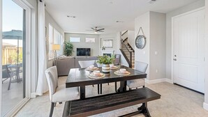 A spacious living area with a dark wooden dining table set for four, a sofa, and a staircase leading to an upper level.