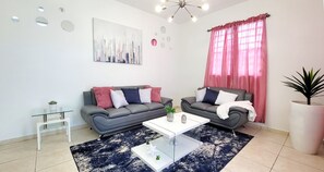 Un salon moderne avec deux canapés gris, une table basse blanche et une grande fenêtre ornée de rideaux roses.
