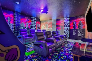 A room with multiple reclining chairs, a patterned carpet, and walls with cityscape murals. - Oasis Villa | 5BR, 4.5 Bath Luxe Home w/ Private Pool, Arcade, and Theater Near Orlando Theme Parks (Kissimmee)