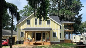 A two-story yellow house with a porch, a covered deck, and a small boat dock. - Waterfront King Beds Pet Friendly Deck Home with Dock & Views. (Eutawville)