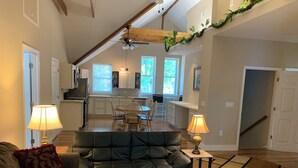 A spacious living area with a black leather sofa, a dining table with chairs, and a kitchen in the background. - Waterfront King Beds Pet Friendly Deck Home with Dock & Views. (Eutawville)