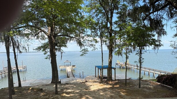 A lakeside view with wooden docks, a covered seating area, and a fire pit. - Waterfront King Beds Pet Friendly Deck Home with Dock & Views. (Eutawville)