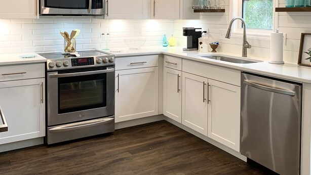Una cocina moderna con armarios blancos, electrodomésticos de acero inoxidable y suelo de madera.
