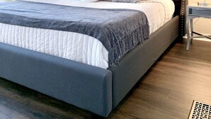 Una cama bien hecha con un cabecero oscuro, almohadas blancas con estampado y una manta gris.