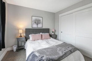 Un dormitorio con cama, una mesita de noche con lámpara, un cuadro en la pared y una puerta blanca.