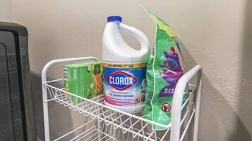 Un chariot contenant des produits de nettoyage, avec une bouteille de désinfectant Clorox, une boîte de liquide vaisselle Gain et un sac de produit nettoyant multi-usages.