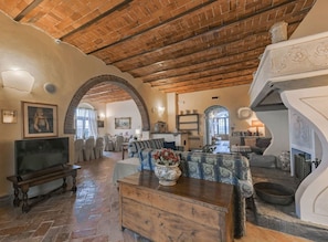 A spacious living room with a high wooden ceiling, a television, a sofa, and a dining area with chairs.