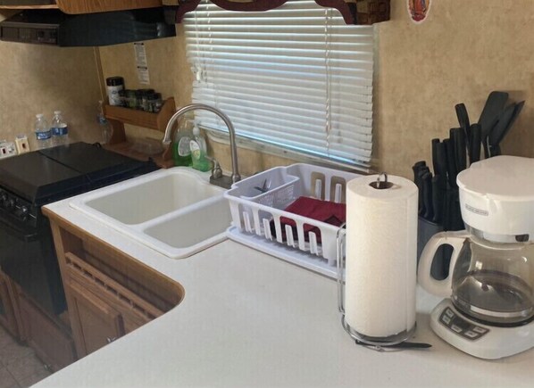 Compact kitchen area with double sink, coffee maker, and storage basket.