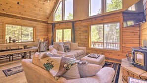 A cozy cabin interior with a high ceiling, wooden walls, and large windows. There is a fireplace, a dining table, and comfortable seating. - Walk to Duck Creek Village: A-Frame Getaway! (Duck Creek Village)