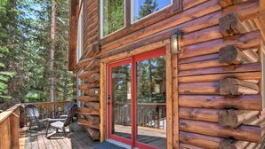 A log cabin with a deck, red-framed glass doors, and a view of the forest. - Walk to Duck Creek Village: A-Frame Getaway! (Duck Creek Village)