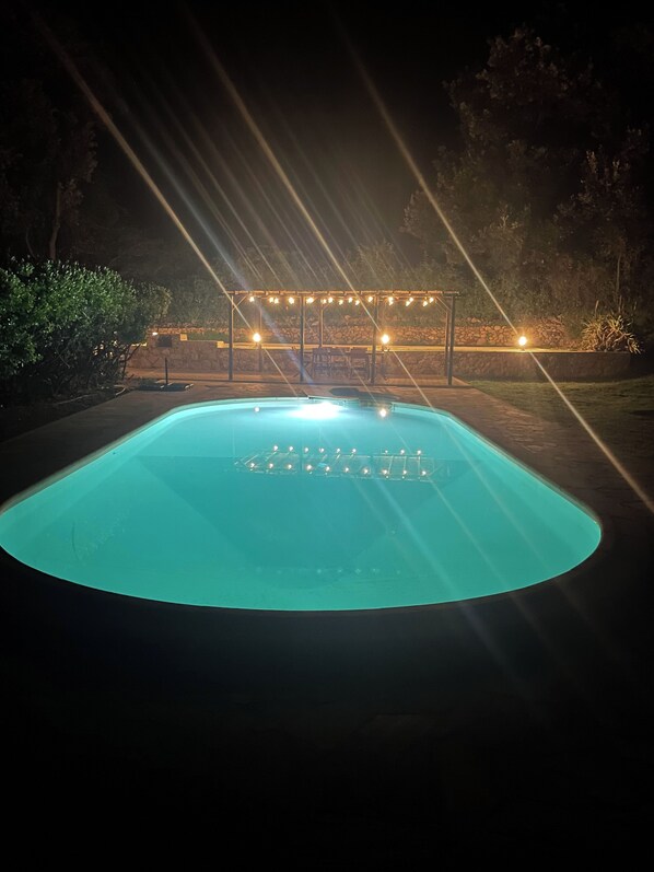 A swimming pool with string lights and a pergola.