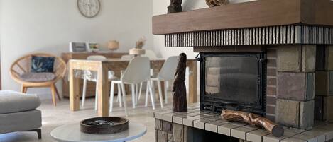 A living room with a stone fireplace, a round coffee table, and a dining area in the background.