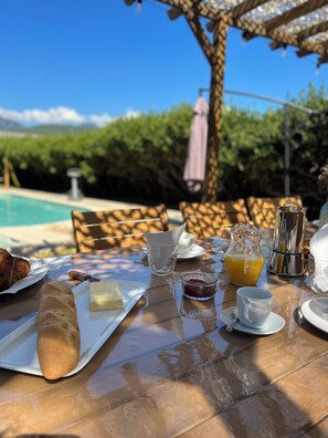 An outdoor dining table with breakfast items, a glass pitcher of orange juice, and a metal coffee pot.