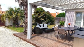 Un patio exterior con zona de estar cubierta, una mesa y una parrilla.
