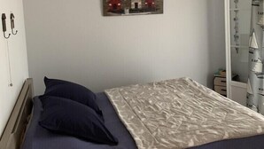 Un dormitorio con cama, almohadas, lámpara colgante, una obra de arte en la pared y un área de ducha con puerta de cristal.