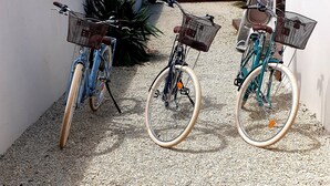 Tres bicicletas estacionadas sobre una superficie de grava, con una pared blanca y un edificio de techo de tejas al fondo.