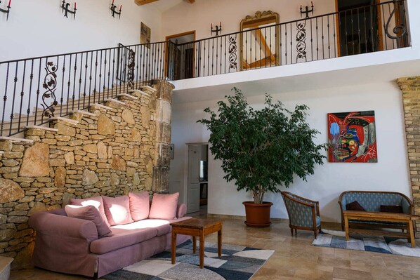 A spacious living area with a stone staircase, a large potted tree, a pink sofa, and a colorful abstract painting. - Mas de la Roncière - Châteauneuf du Pape (Sorgues)