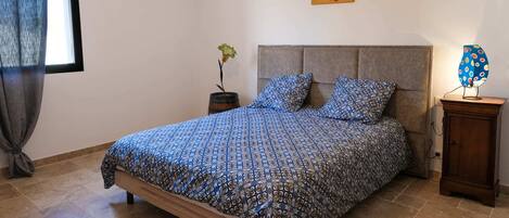 A bedroom with a bed, a nightstand, a lamp, a painting, and a potted plant.