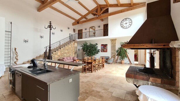 Una cocina amplia con una isla central, un comedor con muebles de madera, una escalera de piedra y una chimenea.