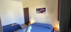 A hotel room with two single beds, a small table with toiletries, a door, and a framed picture on the wall.