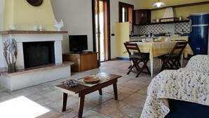 A living room with a fireplace, a television, and a dining area with a table and chairs. - Arimondi cottage with patio and garden (San Vito Lo Capo)