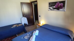 A hotel room with two beds, a door, a framed picture, and a nightstand with a lamp. - Arimondi cottage with patio and garden (San Vito Lo Capo)