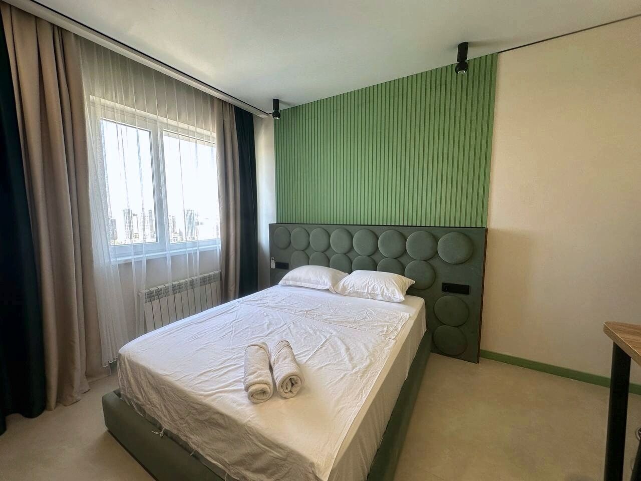 Een hotelkamer met een bed, een hoofdeinde met ronde decoraties, een raam met gordijnen en een radiator.