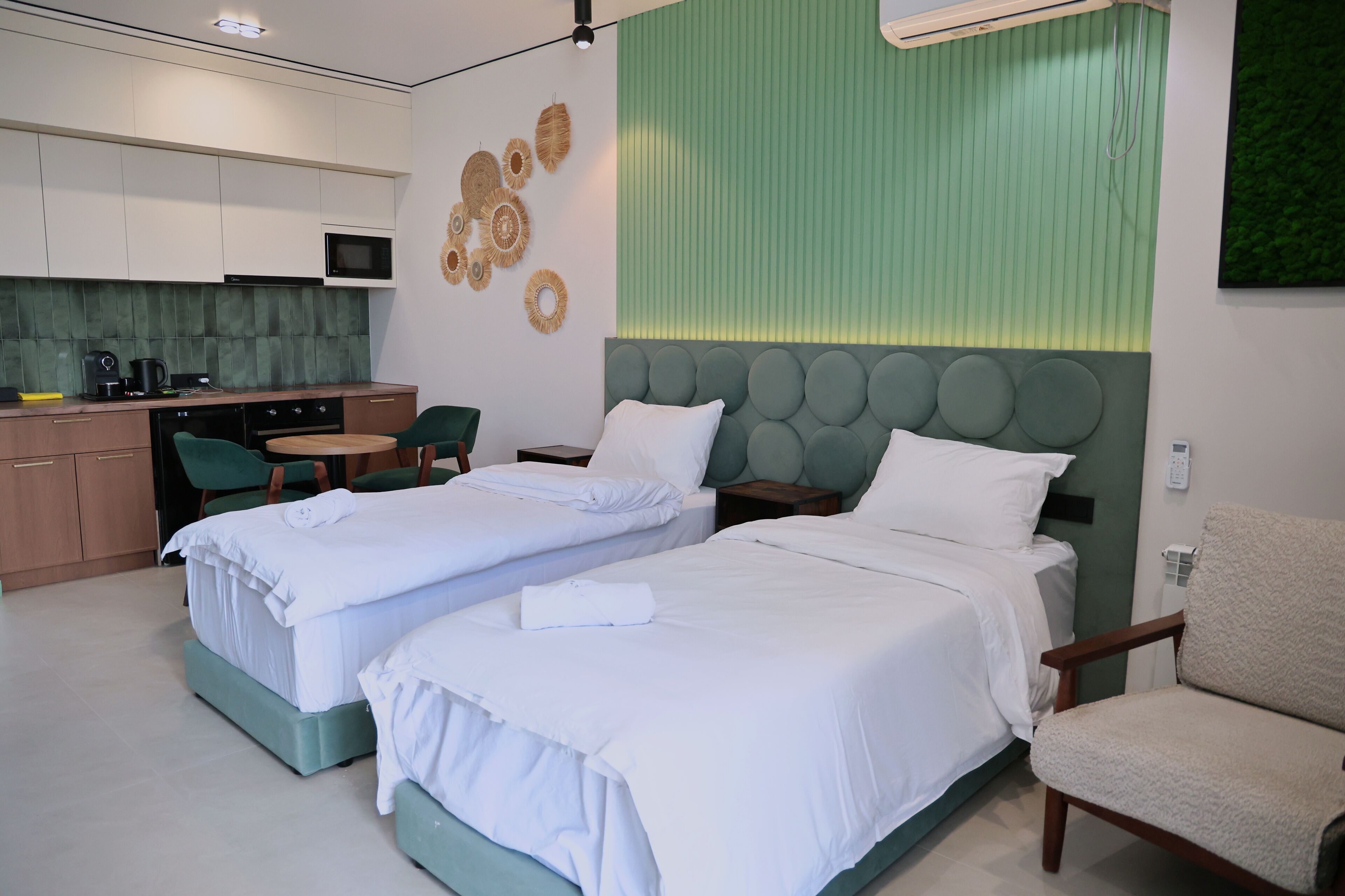 Une chambre d’hôtel avec deux lits, une kitchenette et un mur d’accent de couleur verte.