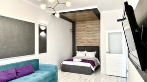 A modern bedroom with a bed, a blue sofa, a wooden accent wall, and a ceiling light fixture. - Prego apartments Almatau (Astana)
