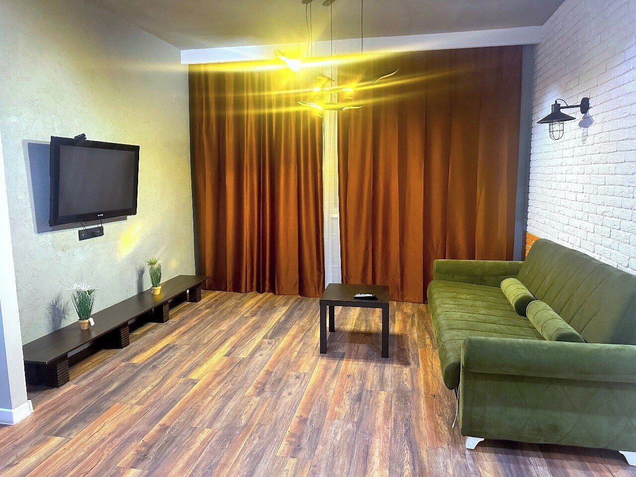 A living room with a flat-screen TV mounted on the wall, a sofa, a coffee table, and a wooden floor.