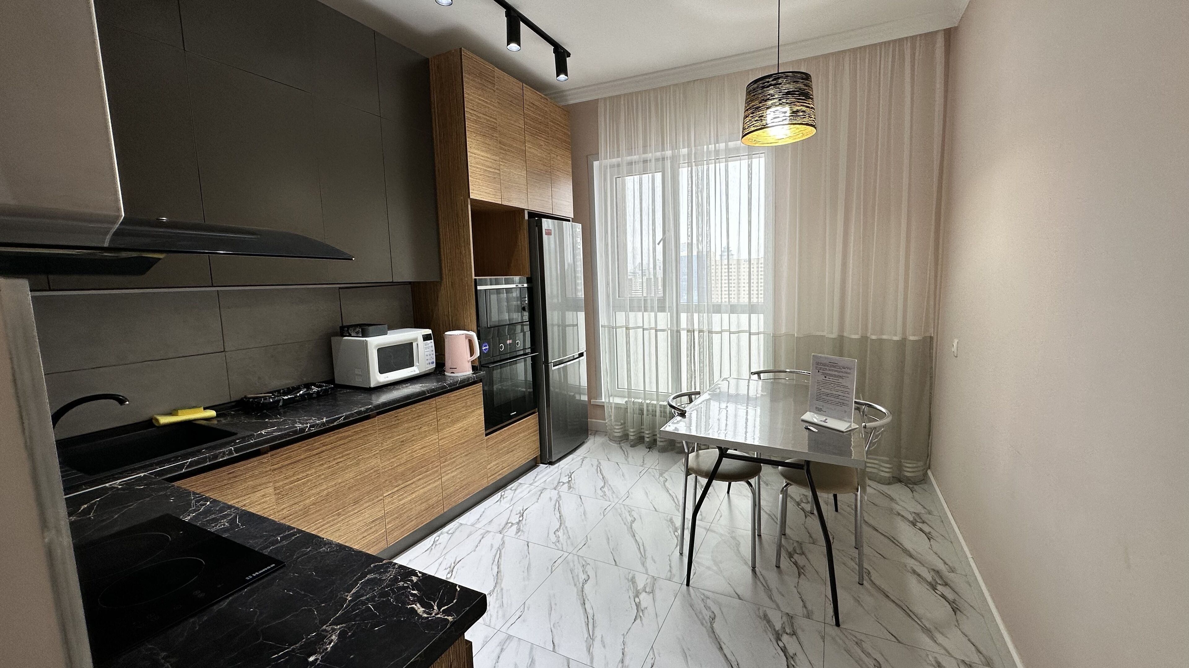A modern kitchen with a black countertop, white marble flooring, and a dining area with a glass table and chairs.