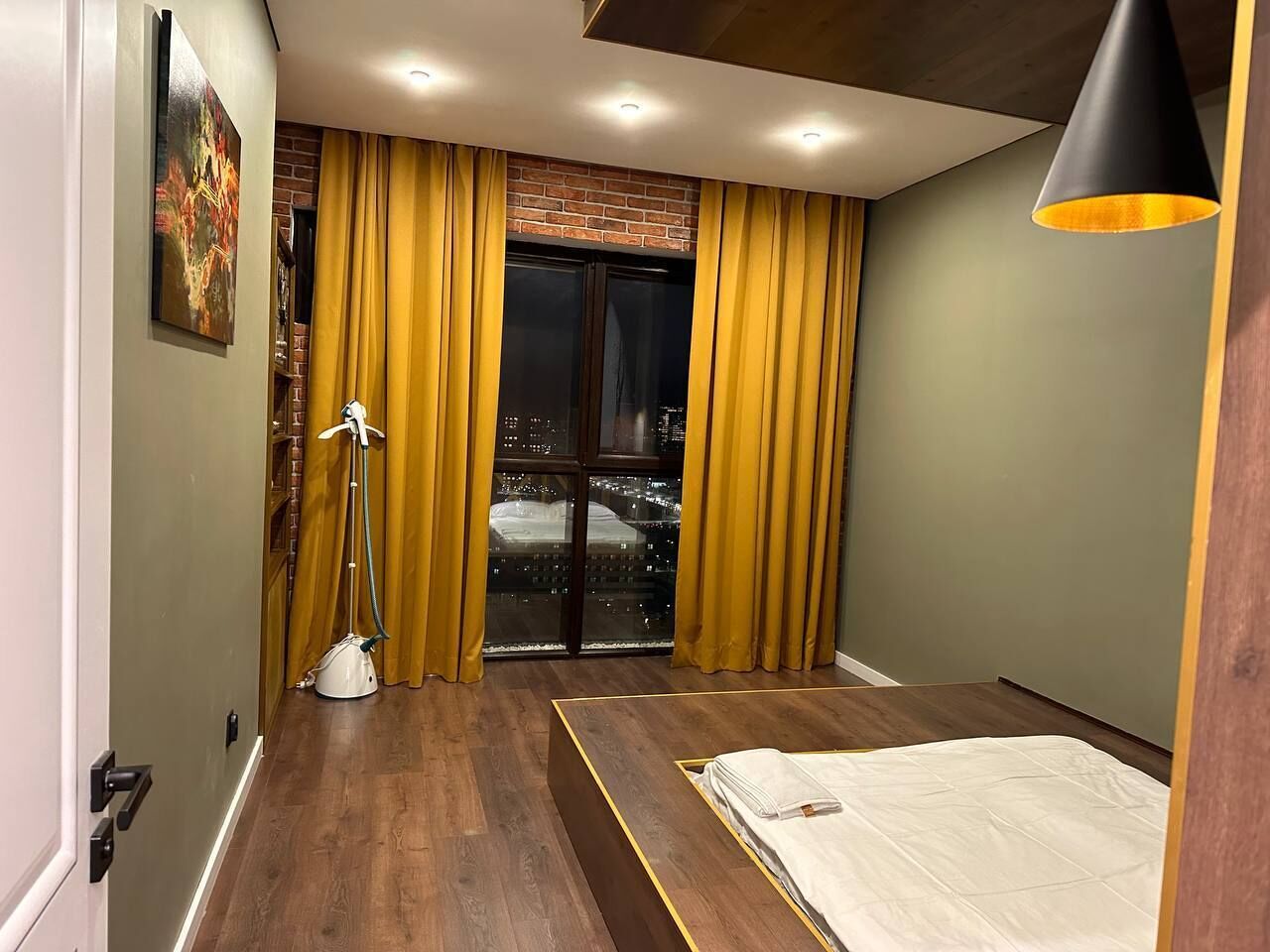 Un dormitorio moderno con un ventanal grande, una cama, un aspirador y vistas a la ciudad.
