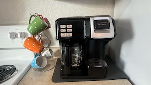 Une machine à café est posée sur un plan de travail dans la cuisine, avec une cuisinière en arrière-plan.
