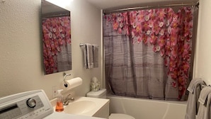 Une salle de bain équipée d’un lave-linge, de toilettes, d’un lavabo et d’un rideau de douche à motifs floraux.