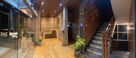 Un moderno vestíbulo de hotel con un mostrador de recepción de madera, una escalera y plantas en macetas.