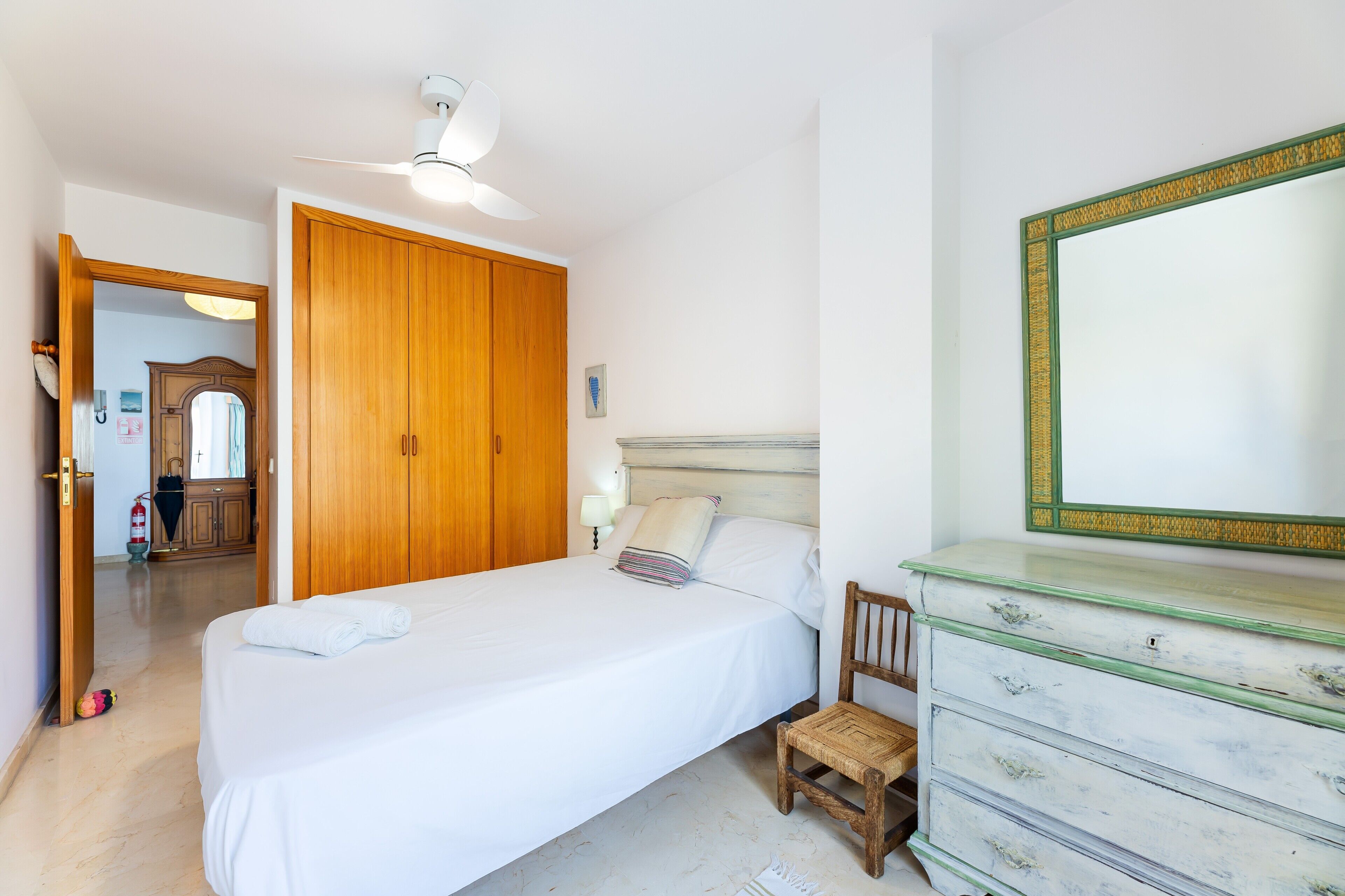 A bedroom with a bed, a dresser, a mirror, and a ceiling fan.