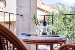 Une table ronde avec une bouteille de vin, deux verres, un livre et une petite plante sur un balcon doté d’une balustrade.