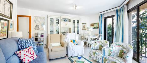 Ein Wohnzimmer mit einer Couch, Sesseln, einem Couchtisch, einem Essbereich und Blick durch große Fenster.