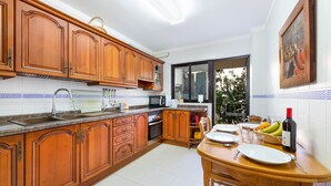 A kitchen with wooden cabinets, a dining table with plates, a bottle of wine, and a window with a view. - Stunning Apartment "Ca Na Bel" with Private Terrace, Balcony & Wi-Fi (Port de Sóller)