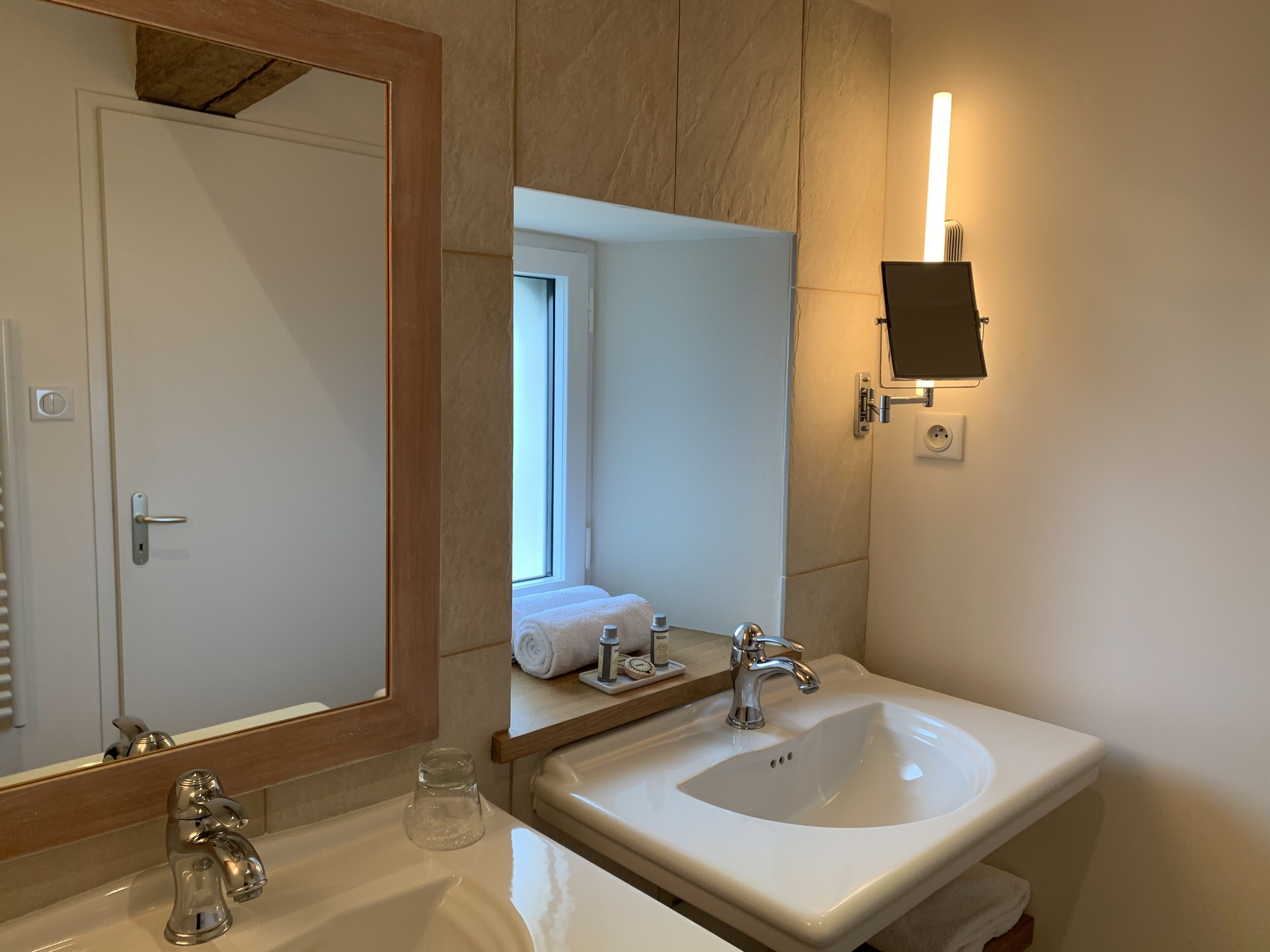 Une salle de bain avec un lavabo blanc, un miroir, un porte-serviettes et un luminaire fixé au mur.