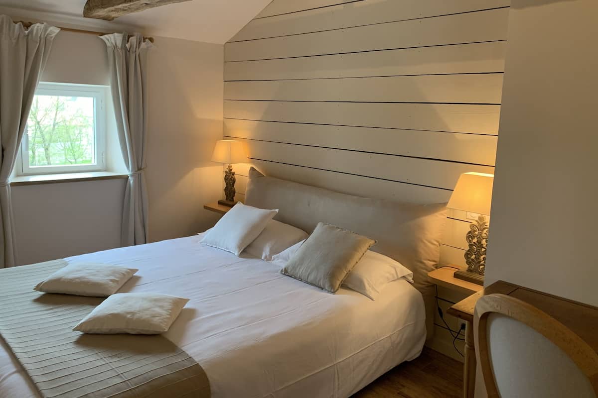 A neatly made bed with white linens and pillows, a wooden headboard, and a bedside table with a lamp.
