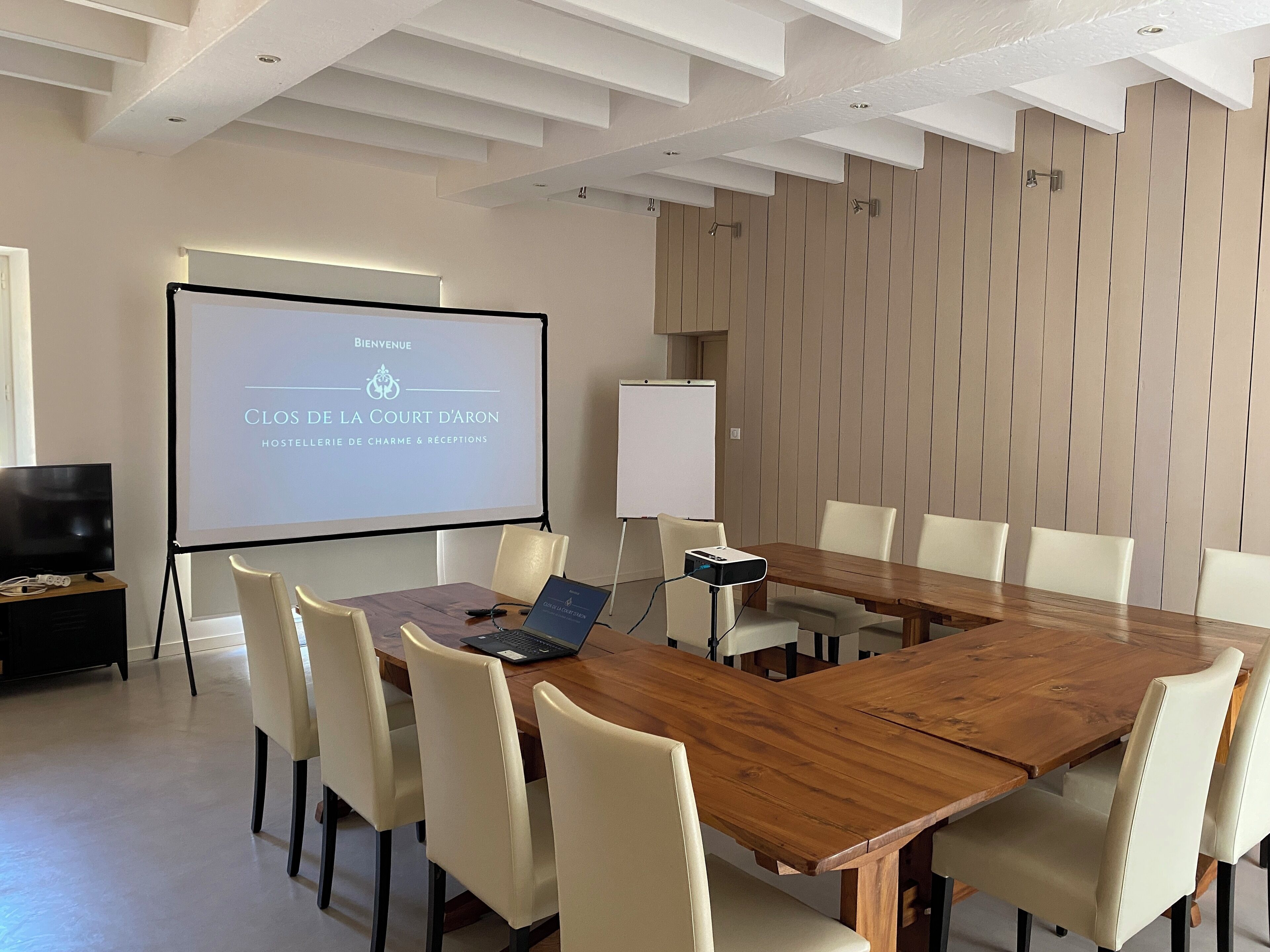A conference room with a wooden table, white chairs, a projector screen displaying a welcome message, and a whiteboard.
