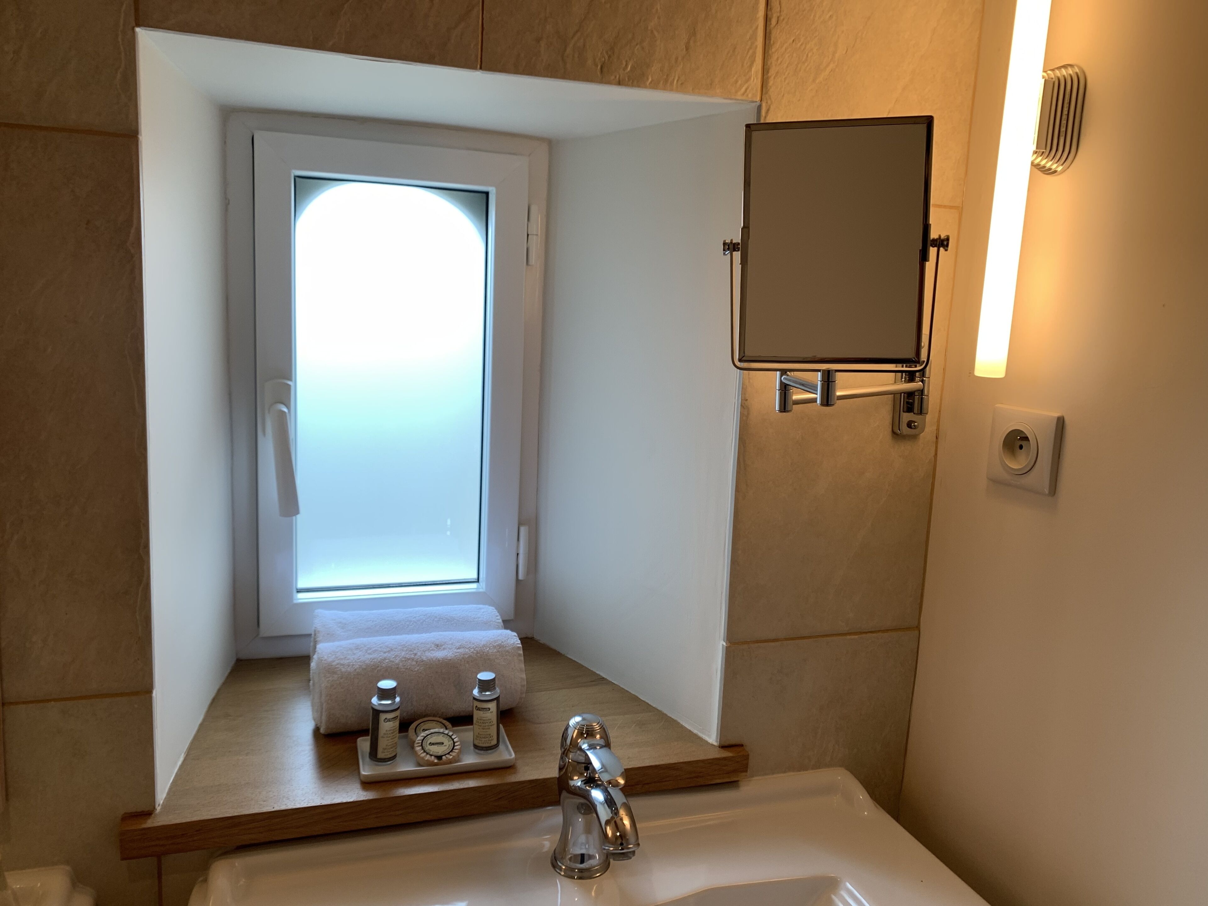 Een moderne badkamer met een ingebouwd raam, een spiegel en een wastafel met toiletartikelen.