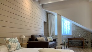 Une chambre avec un grand lit, un canapé sombre, une petite table et un mur en pierre.